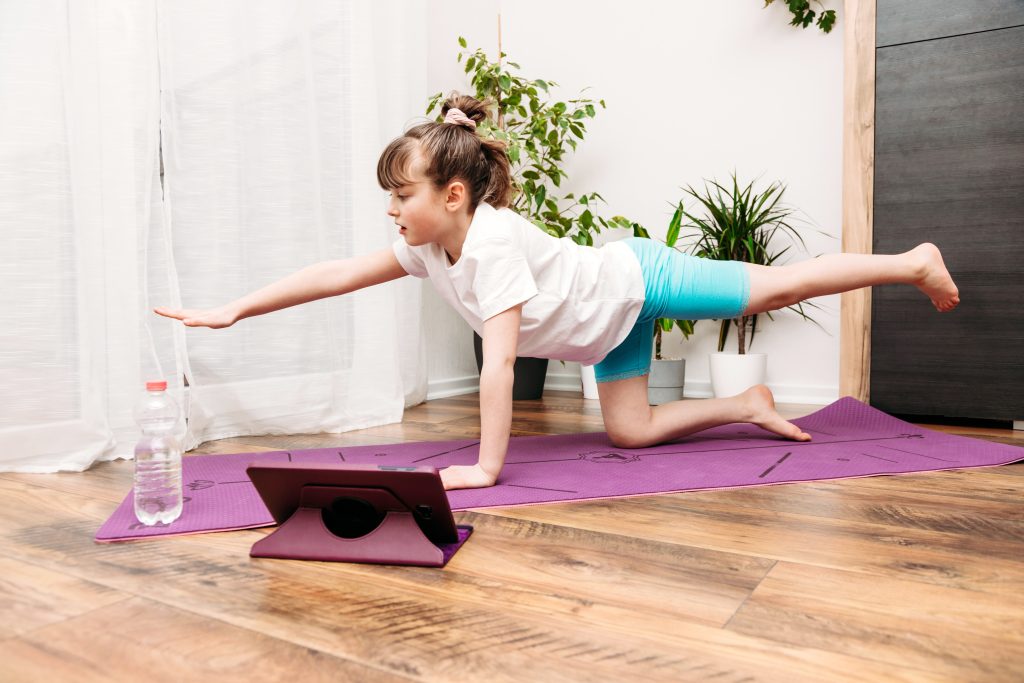 Cute little caucasian girl doing yoga, stretching or gymnastics at home. Fitness for kids online